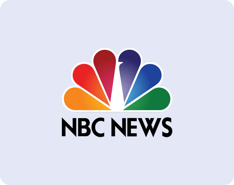 NBC News logo featuring a stylized, multi-colored peacock with six feathers in red, orange, yellow, green, blue, and purple above bold black text that reads “NBC NEWS” on a light gray background.
